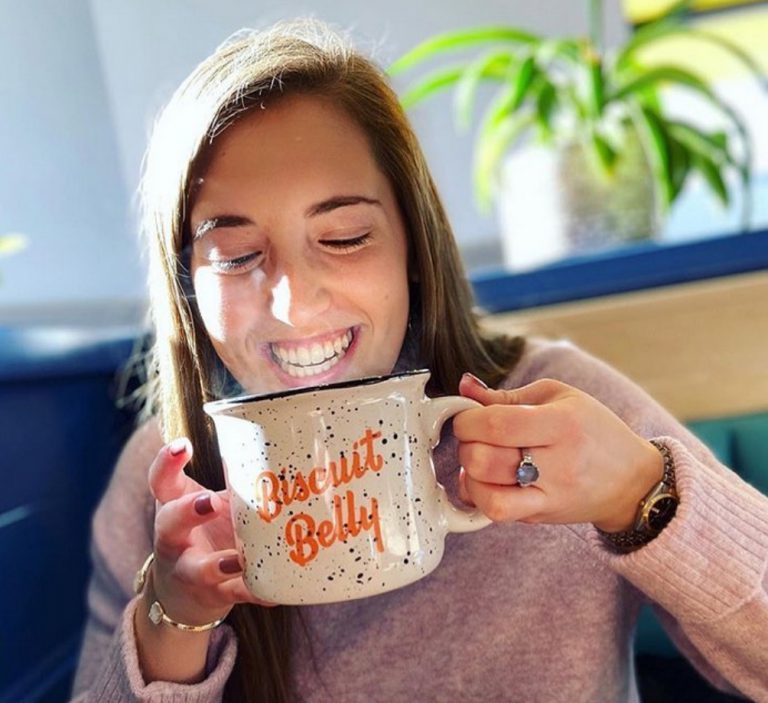 Young brunette woman smiles as she drinks a Biscuit Belly coffee