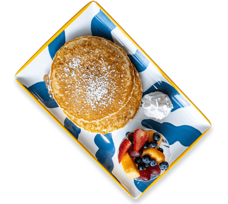 Cut out picture of a stack of pancakes with powdered sugar and a side of fruit on a colorful plate