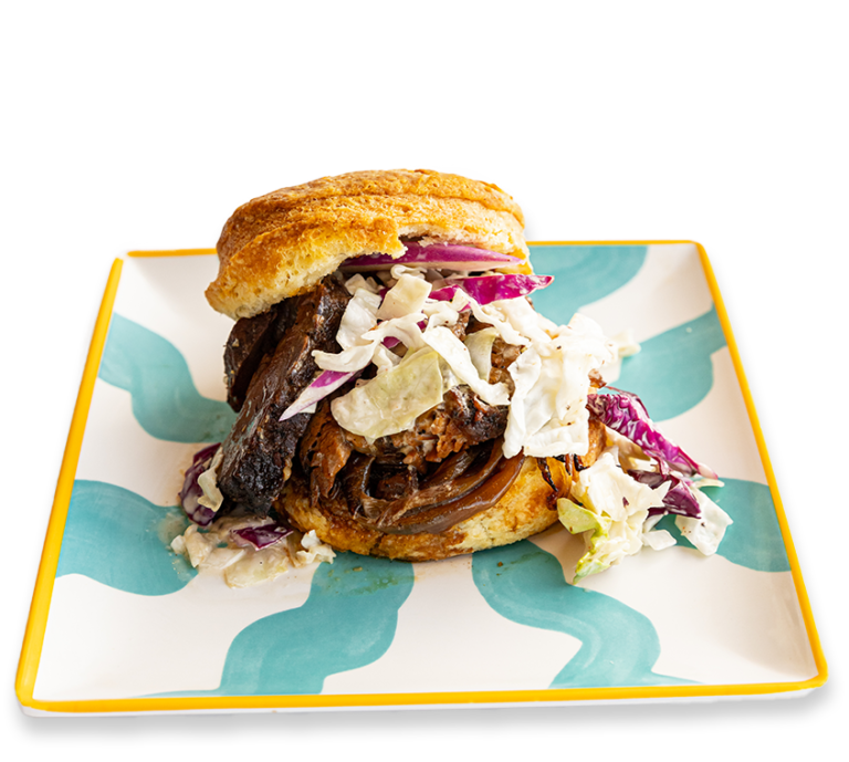 Picture of a Biscuit Brisket sandwich with cabbage slaw and caramelized onions on a colorful plate