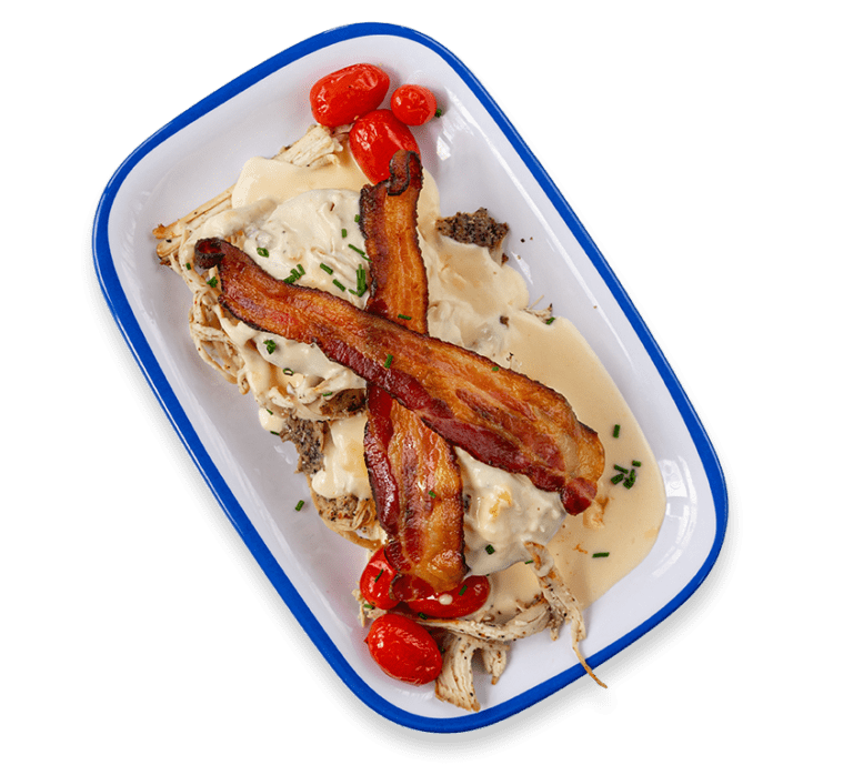 Cut out picture of two biscuits covered in gravy with bacon, turkey, and roasted tomatoes on a rectangular plate