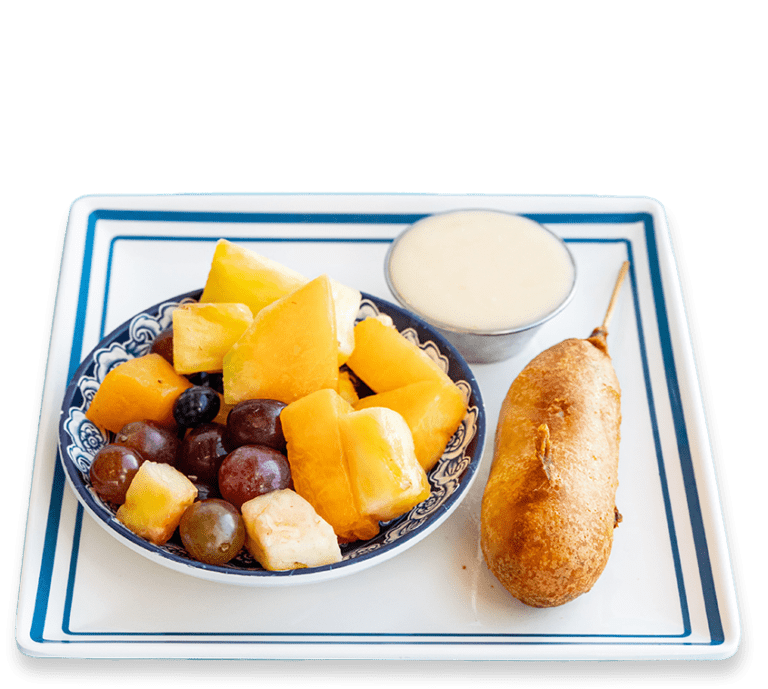 Cut out picture of a kids meal with a pancake corndog, fruit and side of sauce on a blue and white plate