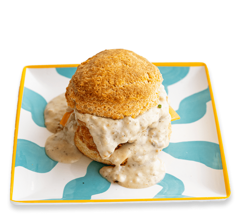 Picture of a biscuit sandwich with gravy, cheese, and fried chicken on a colorful plate