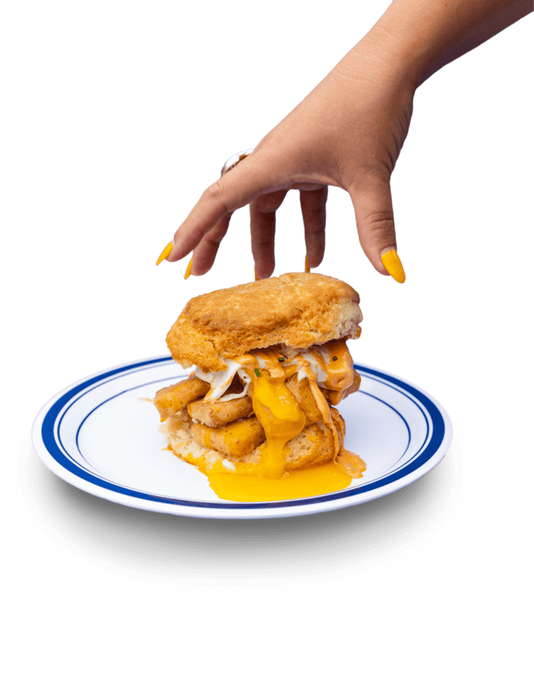 Woman's hand with yellow nails reaching to grab biscuit sandwich with fried eggs