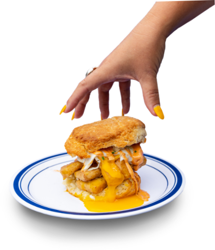 Woman's hand with yellow nails reaching to grab biscuit sandwich with fried eggs