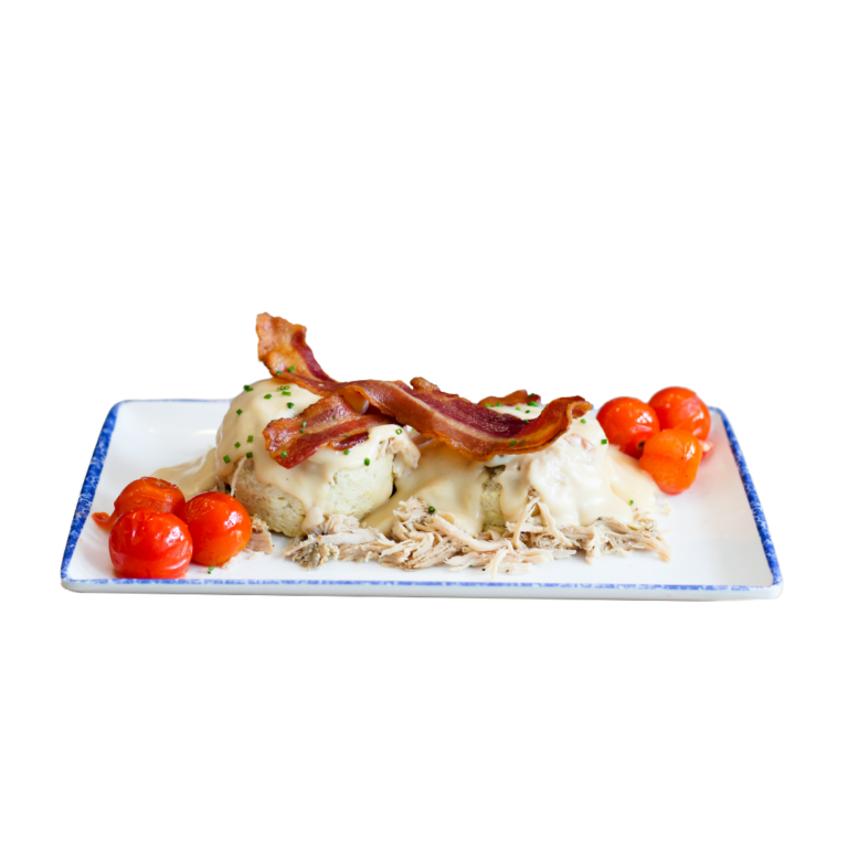 A plate of an open-faced, made-from-scratch biscuit topped with shredded turkey, smoked gouda mornay, two slices of bacon, with roasted tomatoes served in each corner.