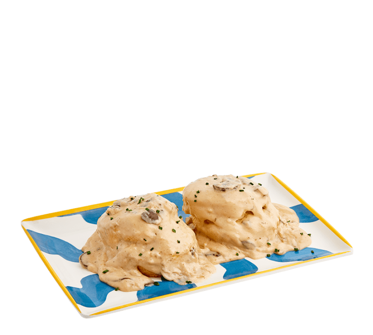 two large scratch-made biscuits topped with mushroom gravy and chopped green chives on a blue and white striped rectangular plate