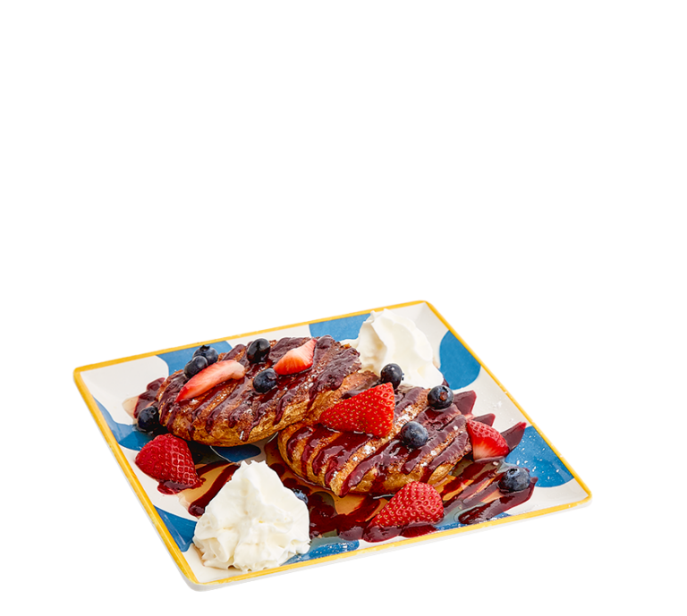 french toast made from flattened biscuits, topped with a drizzle of mixed berry jam, syrup, and topped with strawberries, blueberries and whipped cream on either corner of the blue and white striped plate.
