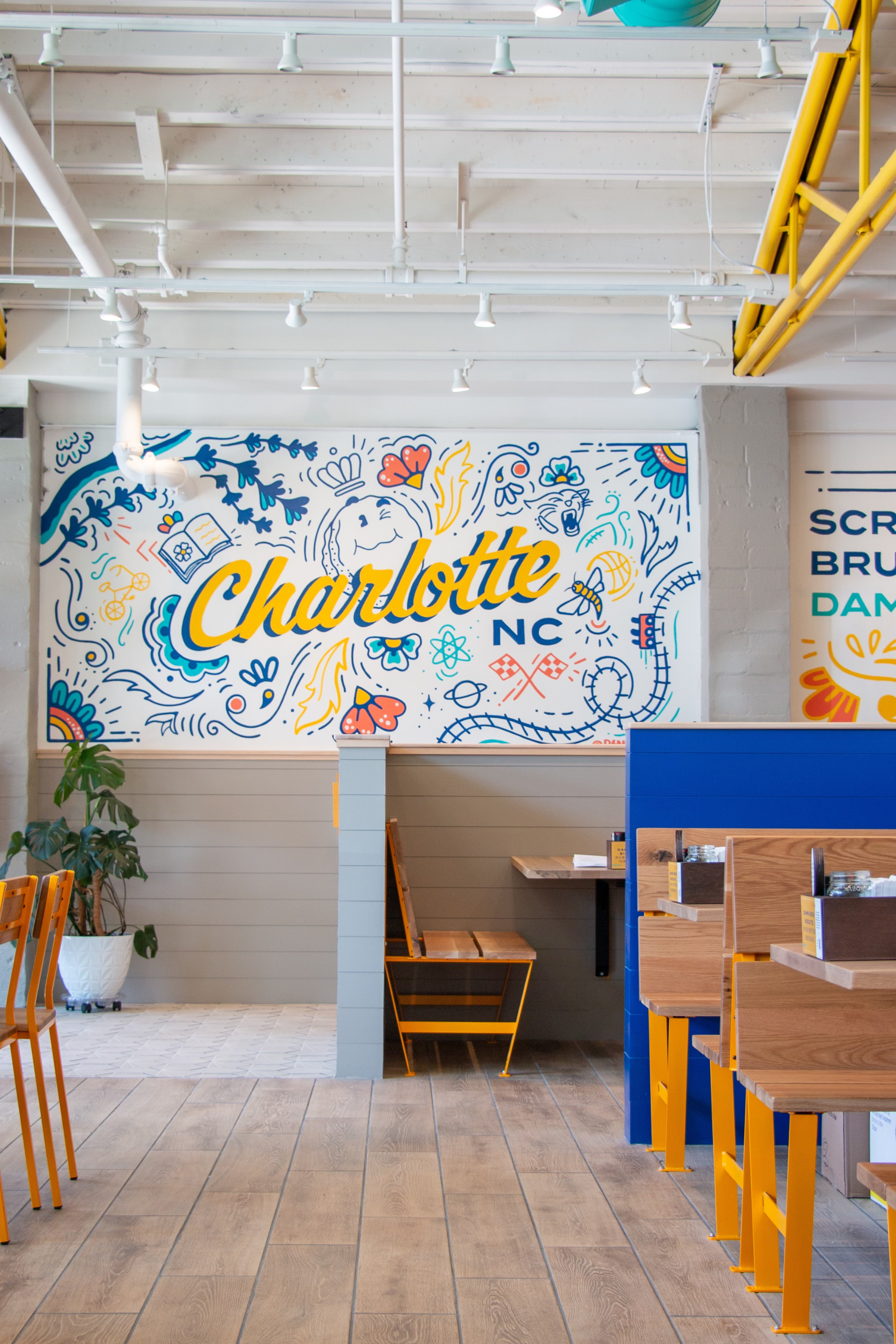An interior image of Biscuit Belly location in Charlotte, NC with a colorful mural that reads "Charlotte, NC" in script letters and surrounded by colorfully painted, local callouts.