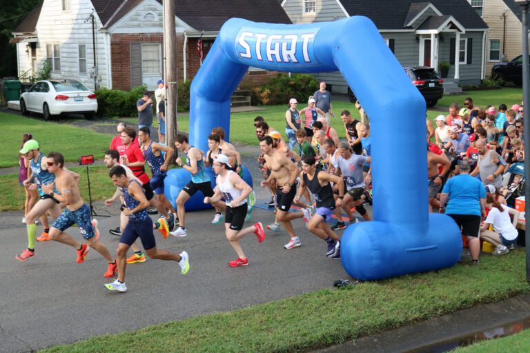 Runners taking under the blue inflatable Start line in neighborhood 5k