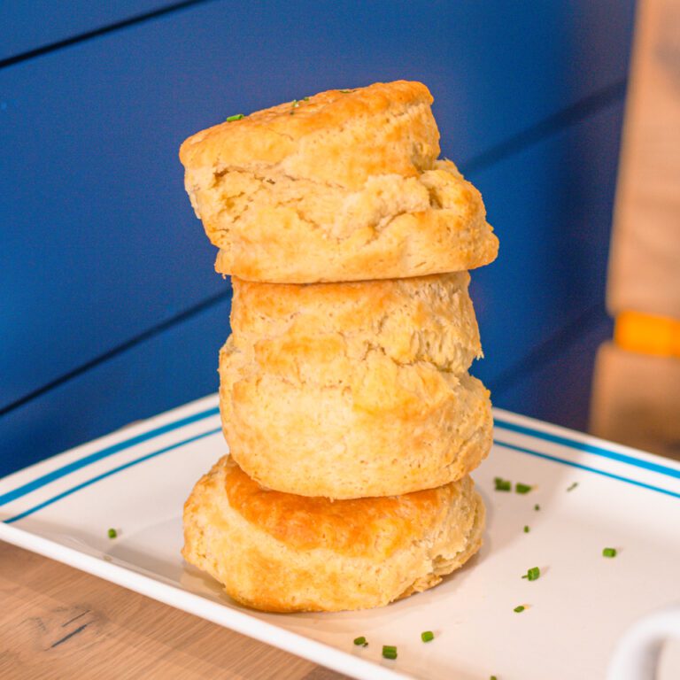 Three Huge Biscuit Belly Biscuits balanced on top of each other on a white plate with blue outline on a wooden table.