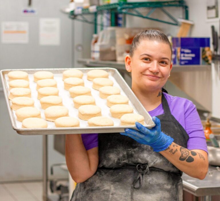 A female baker holds a tray of unbaked biscuits.