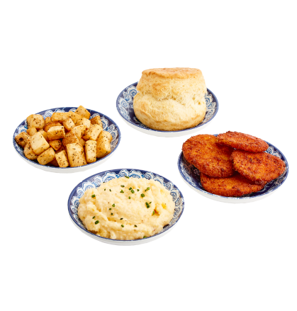 An arrangement of four side dishes - home fries, cheesy grits, fried green tomatoes, and a plain biscuit