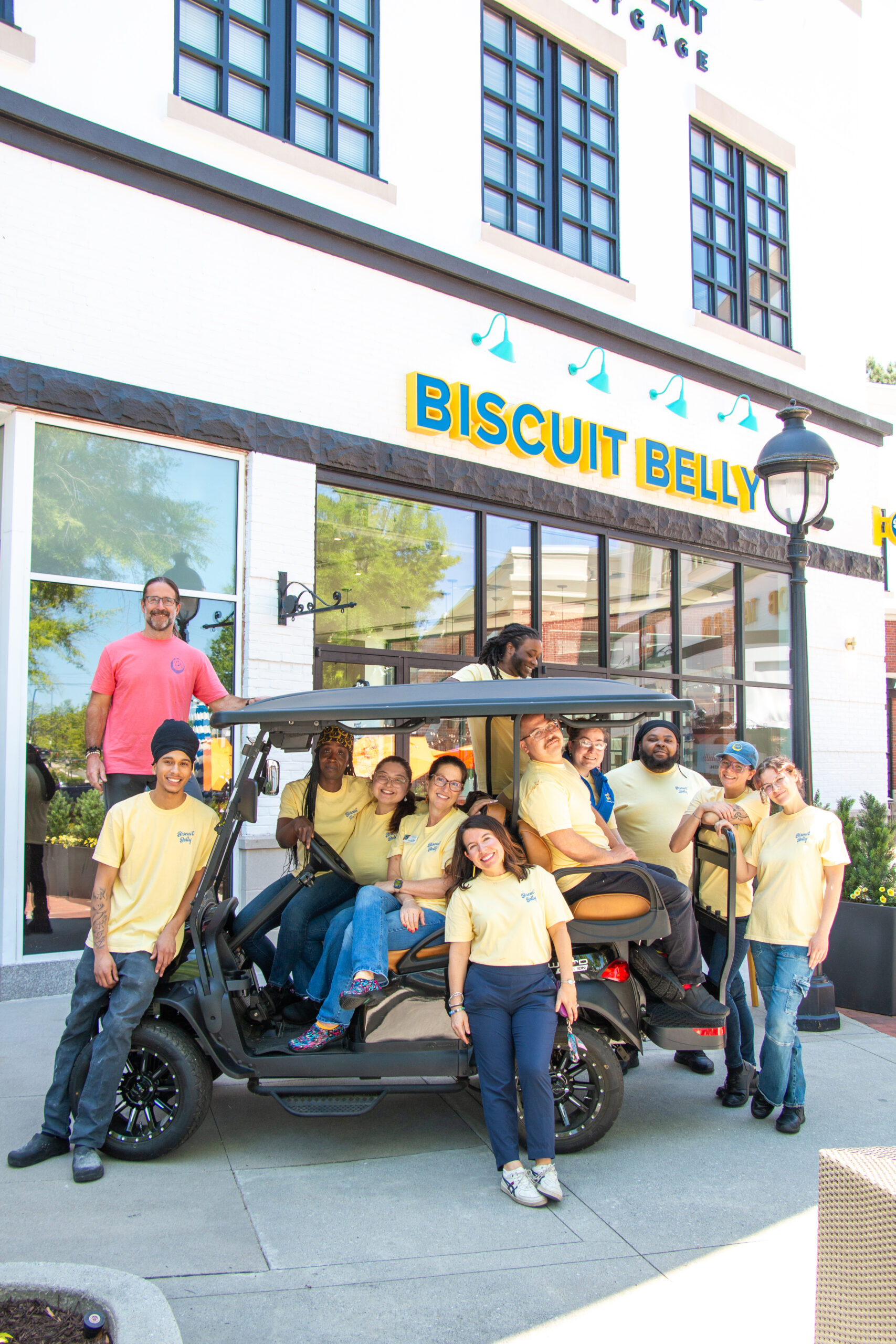 A group of Biscuit Belly employees are piled onto a golf cart in front of the Peachtree City Biscuit Belly location.